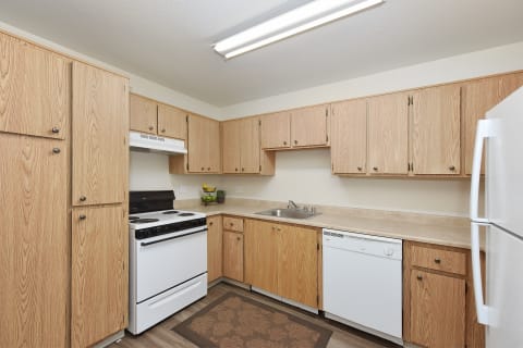 Kitchen area with multiple cabinets for storage, oven, stove, refrigerator, and dishwasher in white.